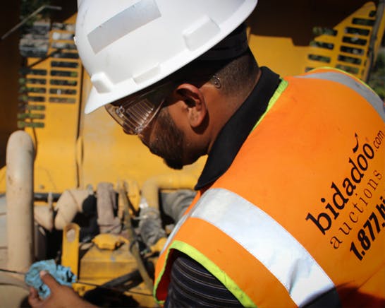 bidadoo Production Lead checking oil level on heavy equipment.